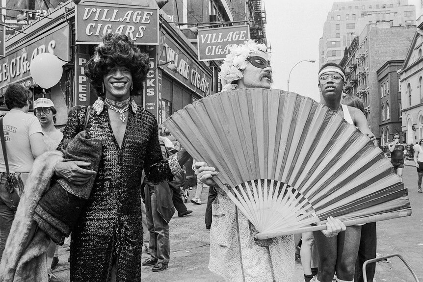 A black and white photo of Marsha P. Johnson dressed in a black sequined gown during the 1982 Pride march in New York.