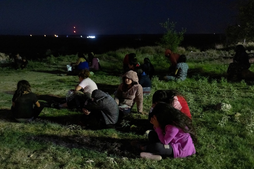 a group of people sitting on the grace at night. 