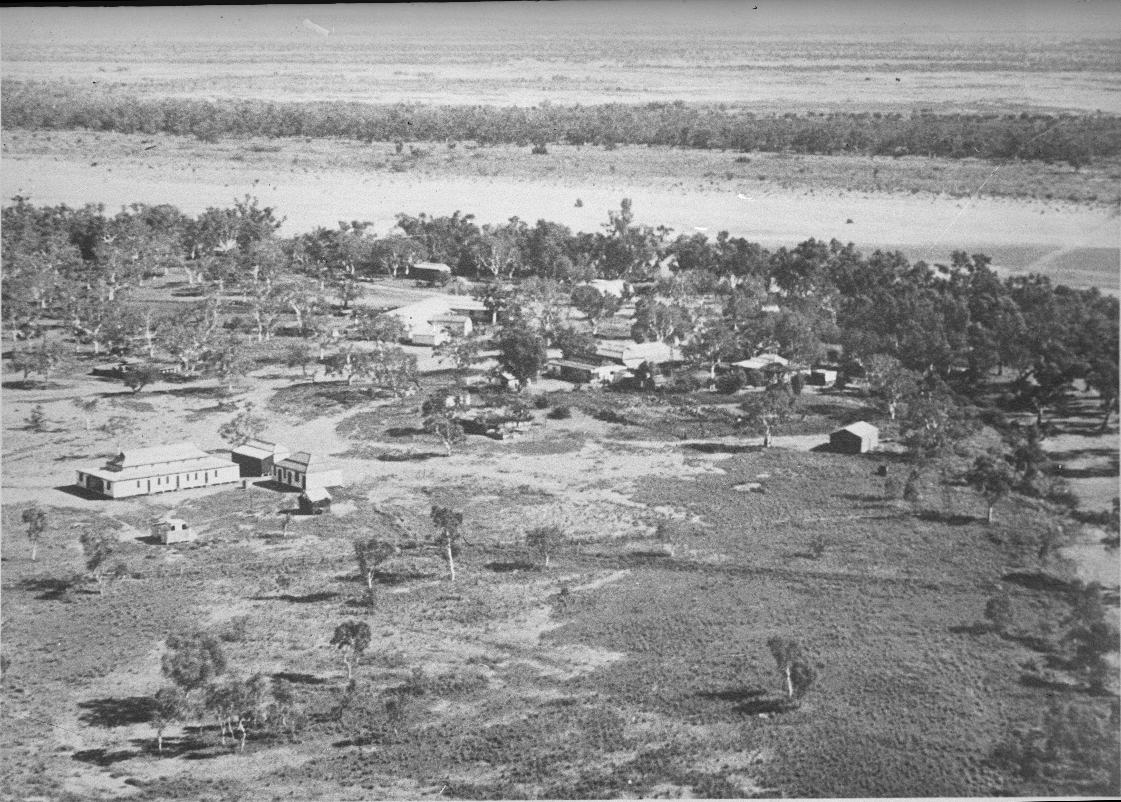Black and white photo of buildings in among trees from above. 