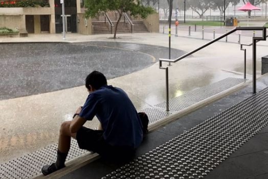 A man attempts to shelter from the rain at southbank, sitting on the steps outside QSO building