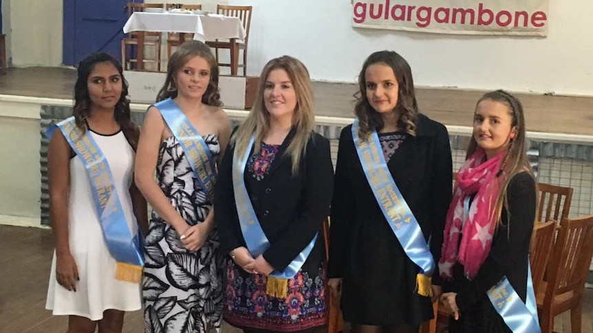 The entrants of the 2017 Gulargambone Showgirl competition stand in a community hall with sashes.
