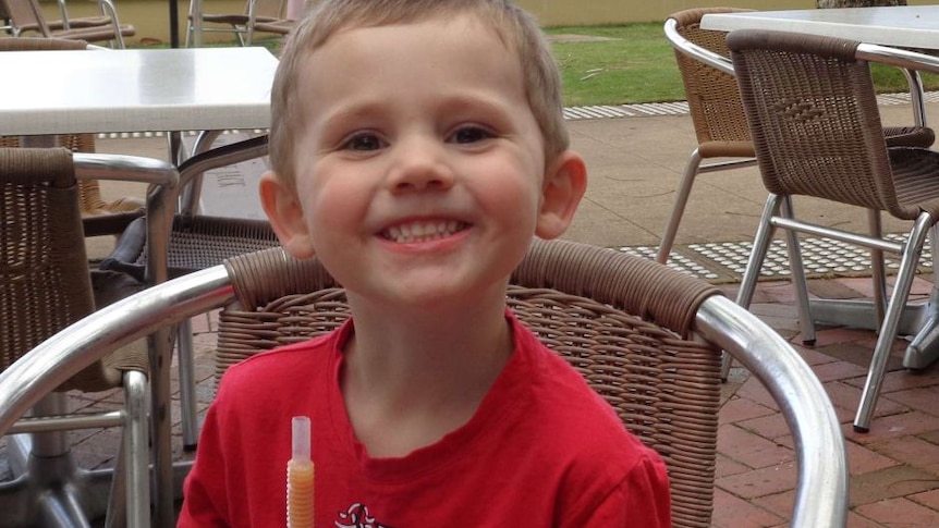 A young boy is smiling in a red t-shirt.