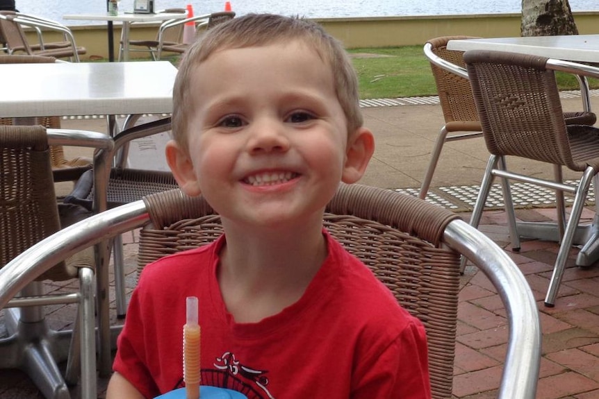 A young boy is smiling in a red t-shirt.