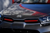 A tightly-cropped image of a grey car bonnet, with a KIA logo on the edge. The bonnet has red accents and the paintwork is shiny