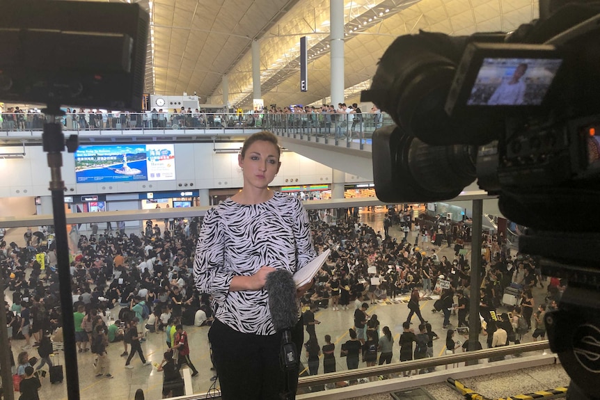 Camera filming Diss standing on level overlooking huge crowd of protesters below.