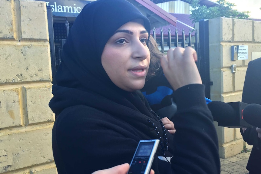 A head and shoulders shot of Zahra Alasadi wearing a hijab and talking to reporters outside a school.