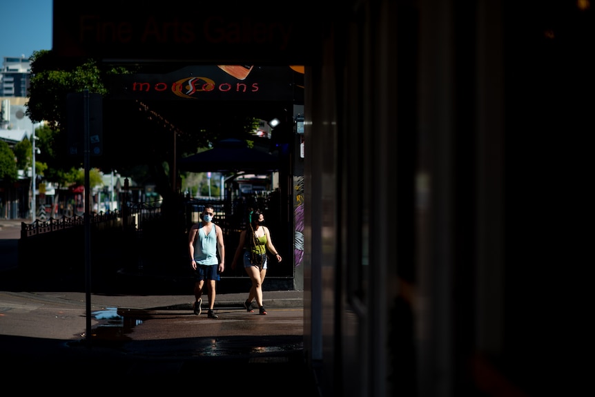 Two people wearing masks walk along a street in Darwin's CBD.