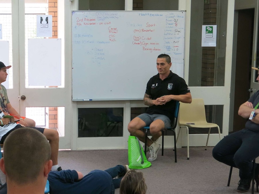Former NRL player PJ Marsh sits in front of whiteboard, young people in foreground listen to him speak