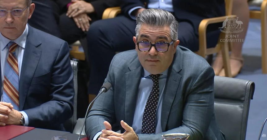 Two men in suits sit a table during a Senate hearing.