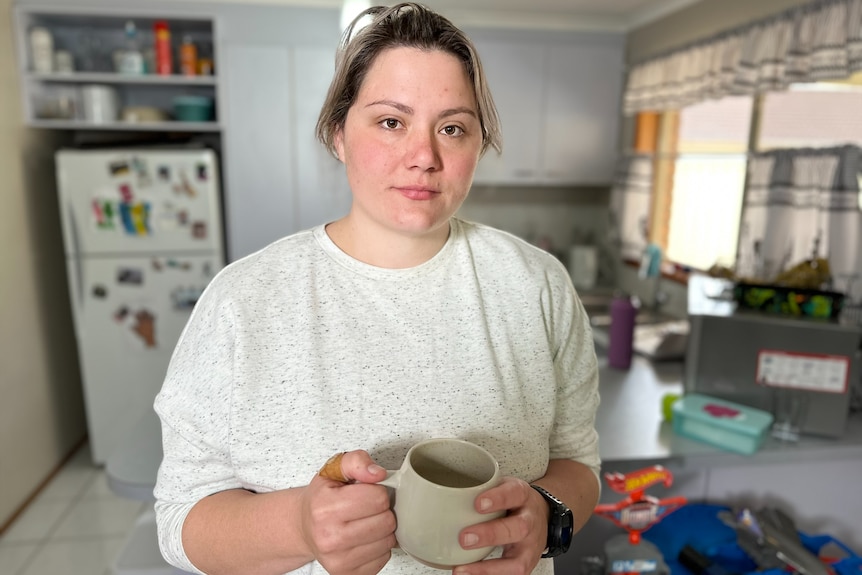 Woman wearing cream coloured top holding a mug. 