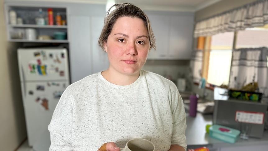 Woman wearing cream coloured top holding a mug. 