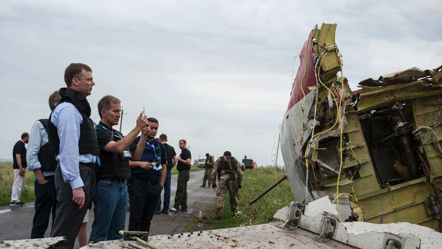 Michael Bociurkiw (C) takes a photo of debris found at the crash site of MH17