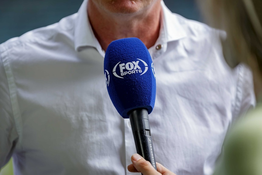 Microphone saying Fox Sports in front of man in business shirt on sports field