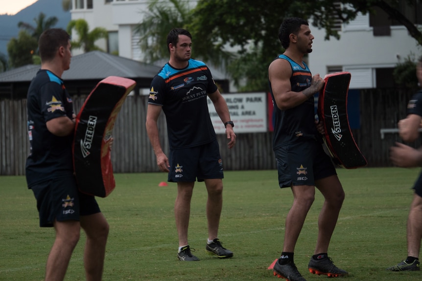 Two young rugby league players with tackle bags while coach watches on.