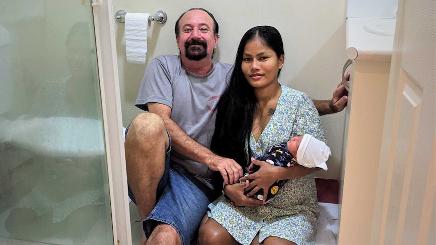 A man and a woman hold a newborn baby in a bathroom, for a story about how to deliver a baby if you don't make it to hospital.