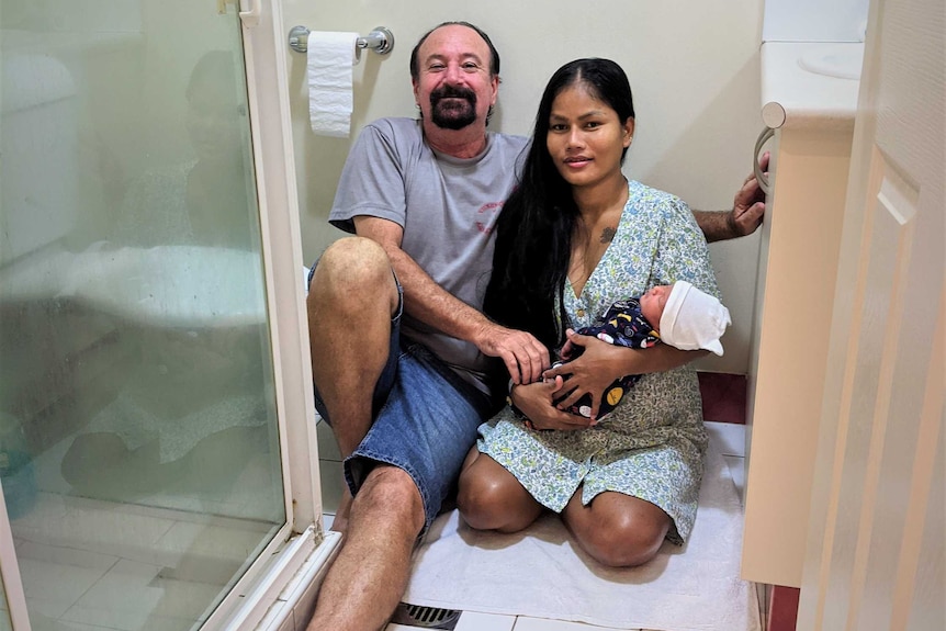 A man and a woman hold a newborn baby in a tiny ensuite bathroom