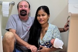 A man and a woman hold a newborn baby in a bathroom, for a story about how to deliver a baby if you don't make it to hospital.
