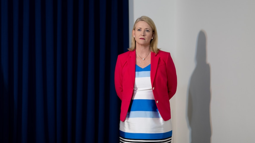 a blonde woman wearing a red blazer and a blue and white dress