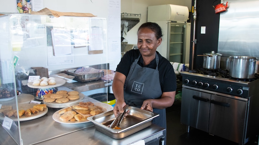 Sudanese woman preparing big platters of food in kitchen.