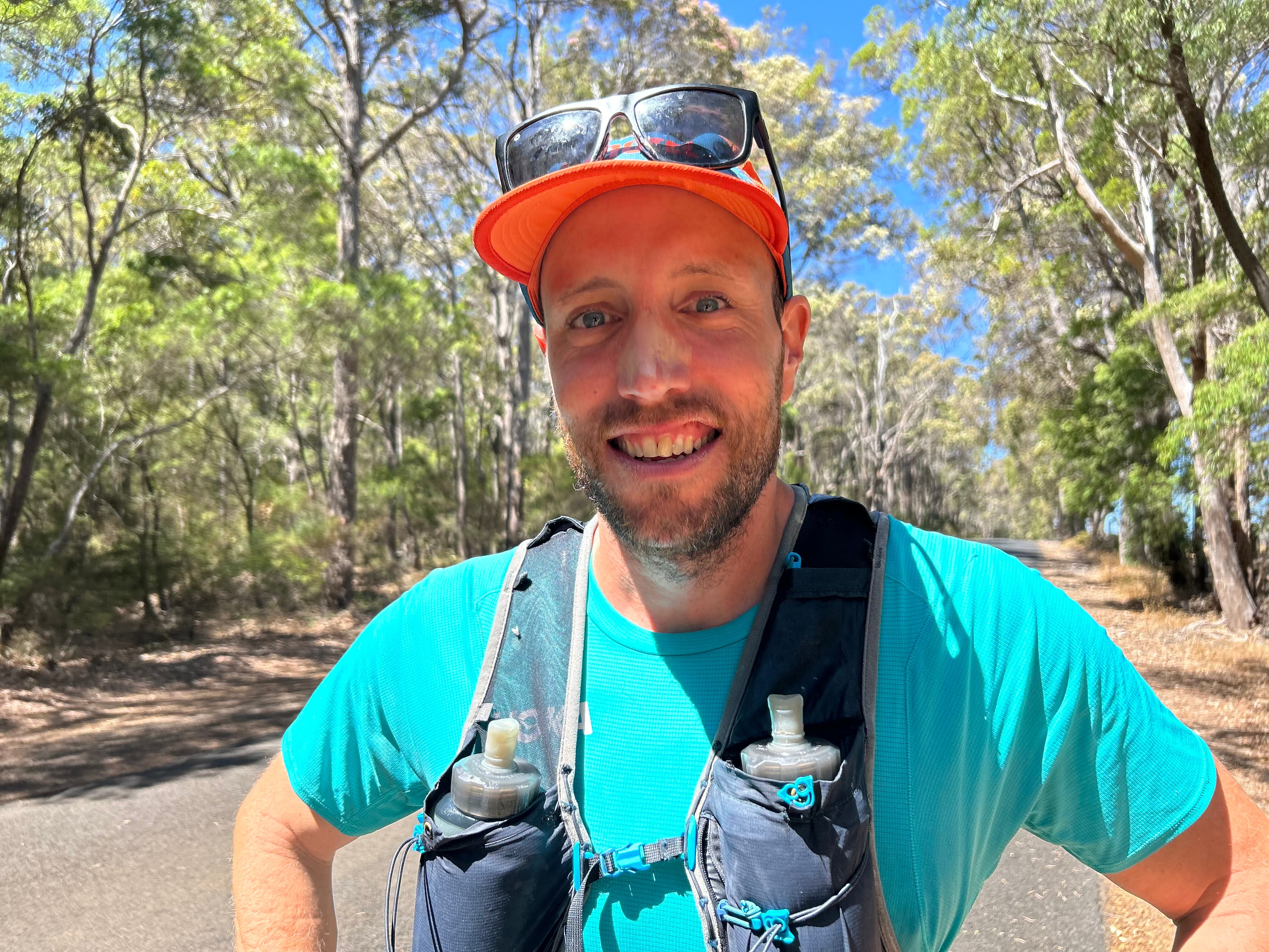Man in orange cap with black sunnies on his head, wearing a bright blue t-shirt, smiles at camera with zinc on his nose.
