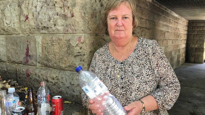 Beverley Marshall holds a plastic water bottle while standing next to a small collection of containers at her Brisbane home.