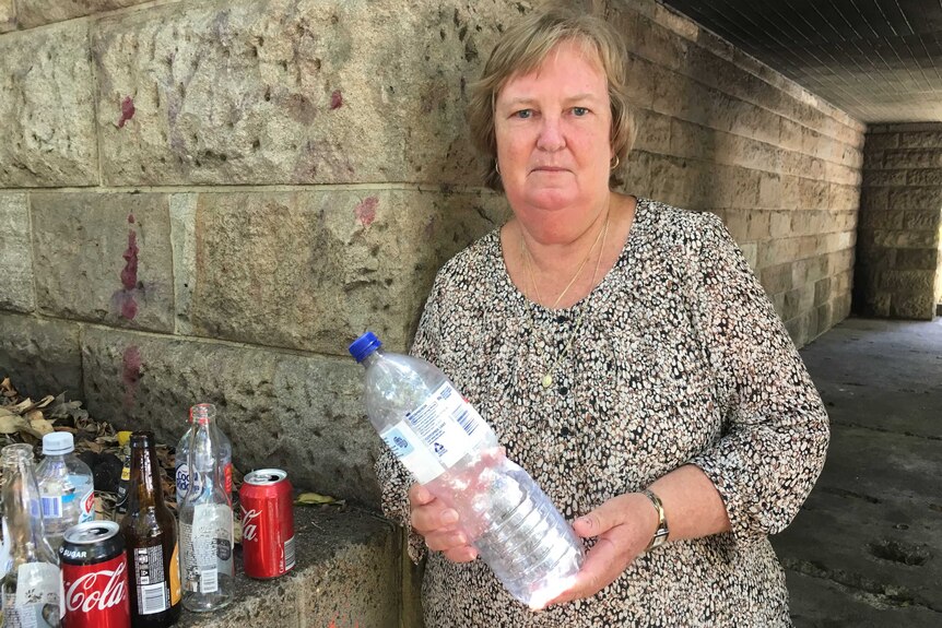 Beverley Marshall holds a plastic water bottle while standing next to a small collection of containers at her Brisbane home.