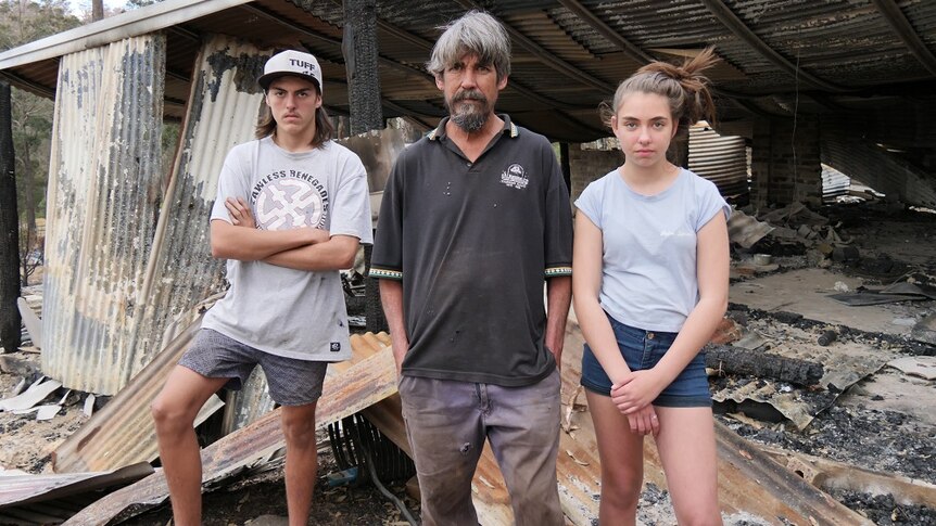 A man, a boy and a girl stand in front of their burnt-out home.