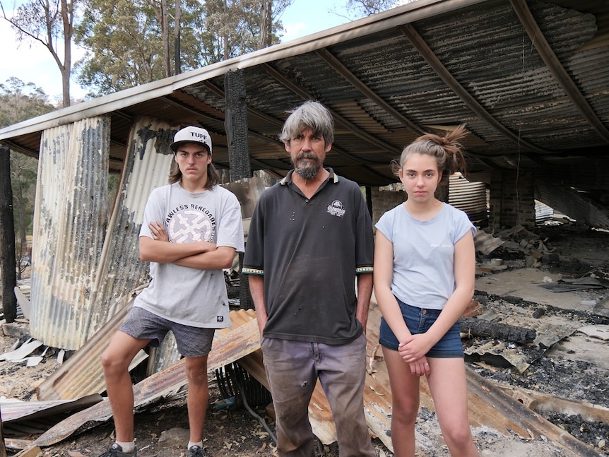 A man, a boy and a girl stand in front of their burnt-out home.