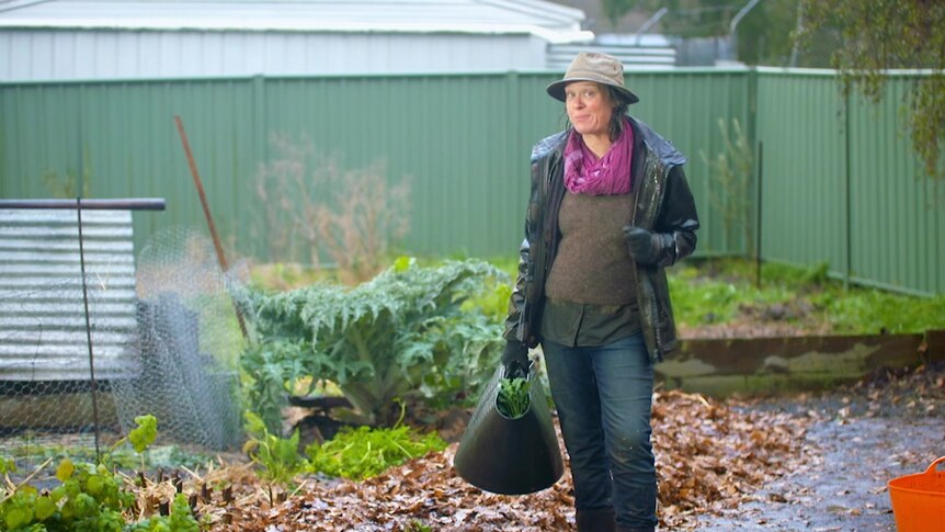 Gardening Australia's Millie Ross holding a bucket in the rain.