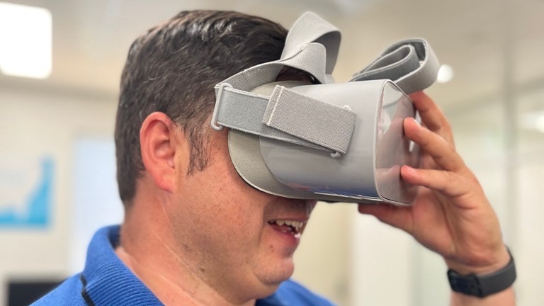 Man in blue polo hold grey virtual reality headset over his eyes 
