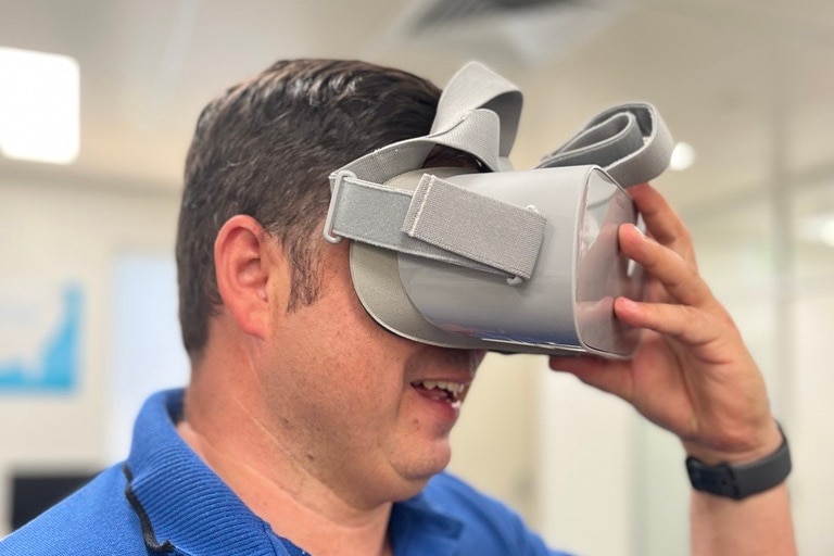 Man in blue polo hold grey virtual reality headset over his eyes 