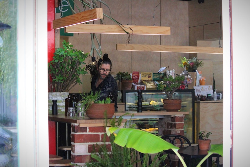 A man wipes tables inside a suburban cafe