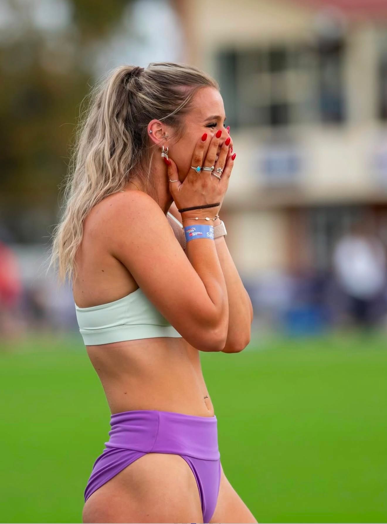 A young woman in running gear puts her hands to her face while standing on a track.