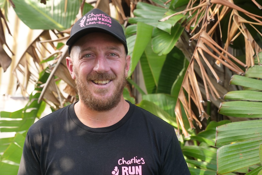 Cheyne Waddingham wearing a cap smiling in front of a banana tree 