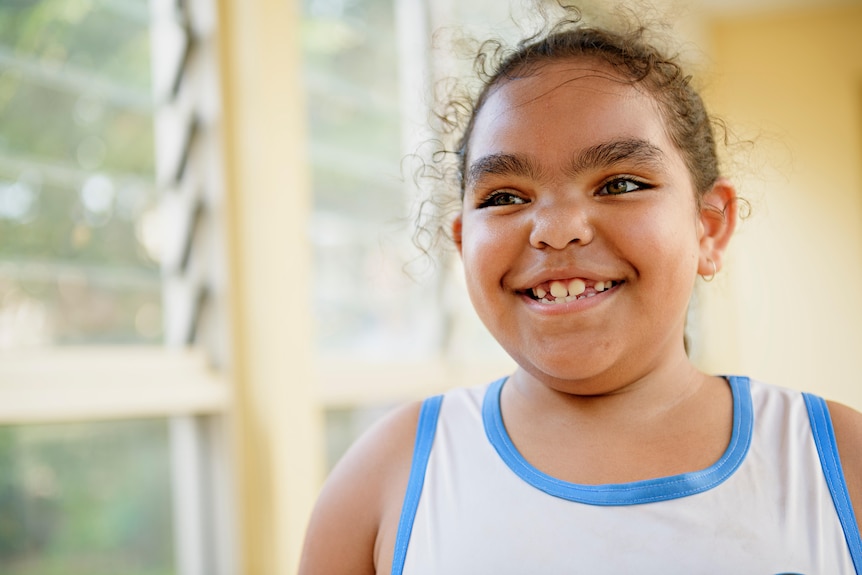 A young girl smiles and looks slightly off camera. She is wearing basketball clothing.