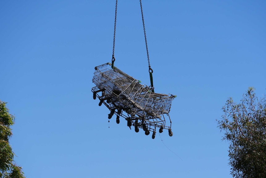 A group of several shopping trolleys are suspended above the ground by a crane