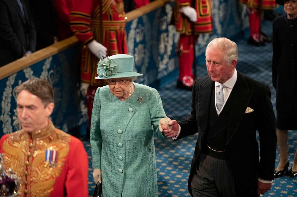 Queen Elizabeth II, in a green suit and hat, and Prince Charles in a black morning suit, walking to the throne.
