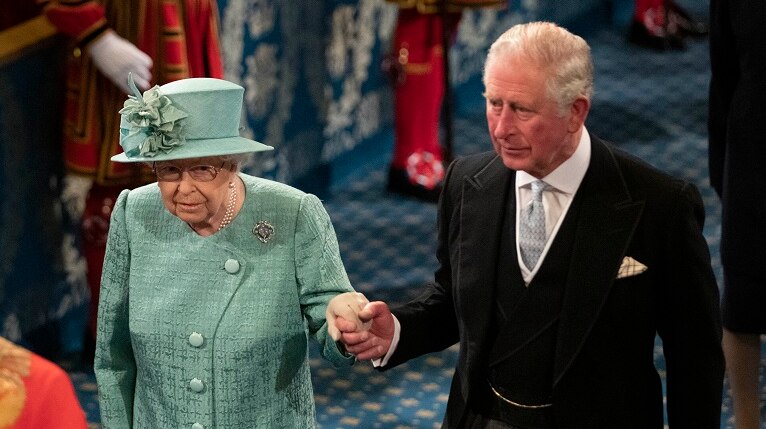 Queen Elizabeth II, in a green suit and hat, and Prince Charles in a black morning suit, walking to the throne.