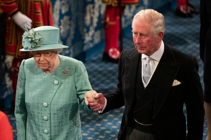 Queen Elizabeth II, in a green suit and hat, and Prince Charles in a black morning suit, walking to the throne.