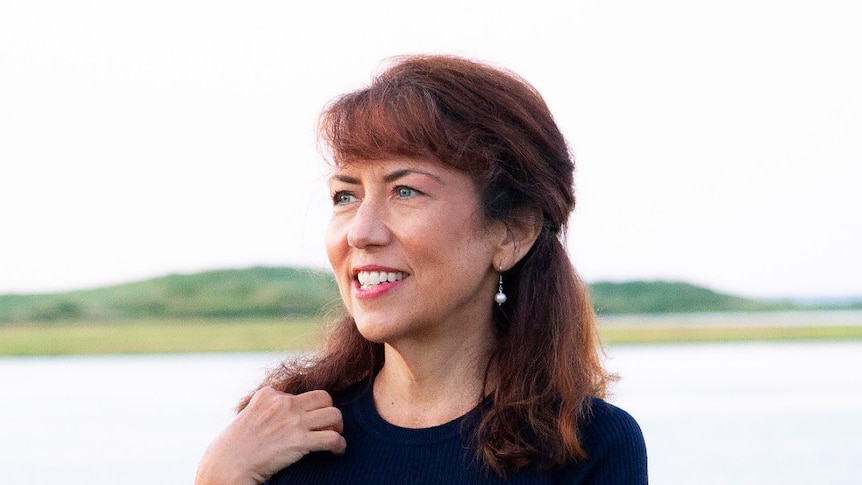 A woman with dark hair stands by a lake.