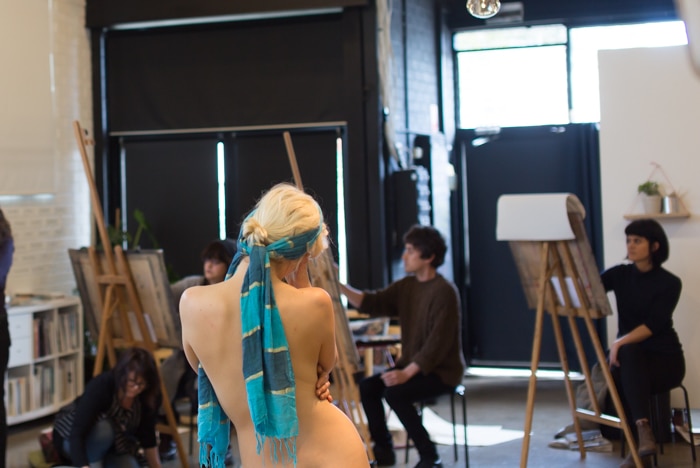 A naked woman poses in front of a life drawing class.