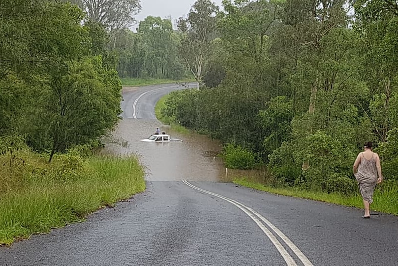 A woman walks towards a car stuck in flood waters at Gympie