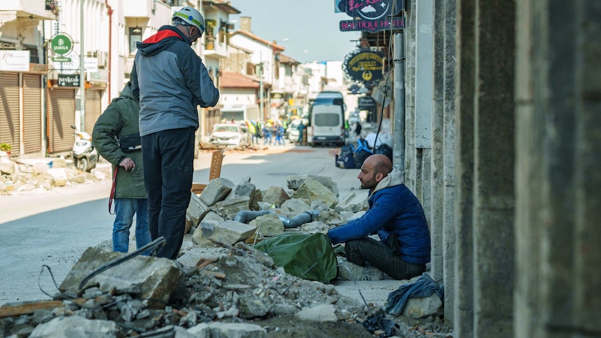 A man crouches down next to a tarp while men in hard hats look down at him