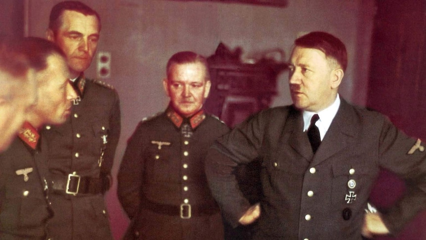 Three German generals in uniform standing next to Adolf Hitler who has his hands on his hips