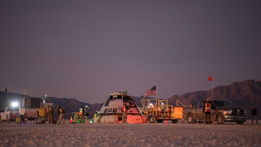 Boeing personnel work around the Boeing Starliner spacecraft shortly after it landed in the desert.