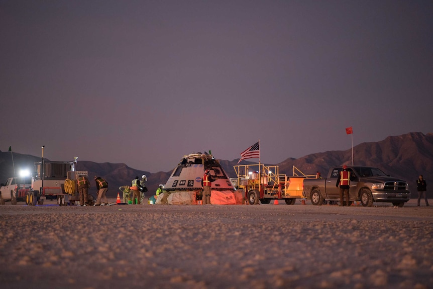 Boeing personnel work around the Boeing Starliner spacecraft shortly after it landed in the desert.