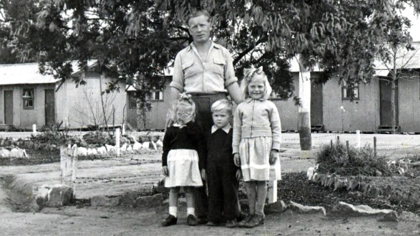 Black and white photo of a European man with his three children in front of accommodation