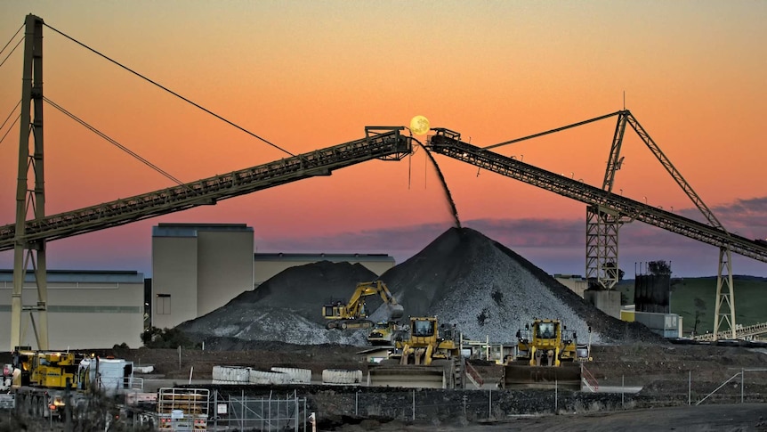 Two mine conveyors frame a full moon at sunset.