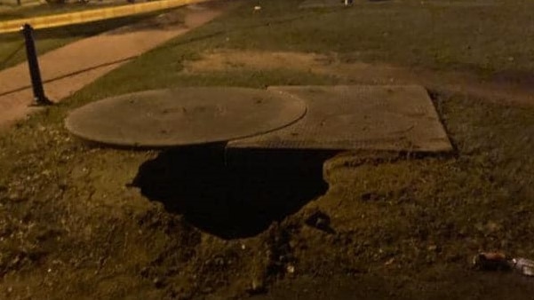 A large sinkhole in the ground near a pathway.