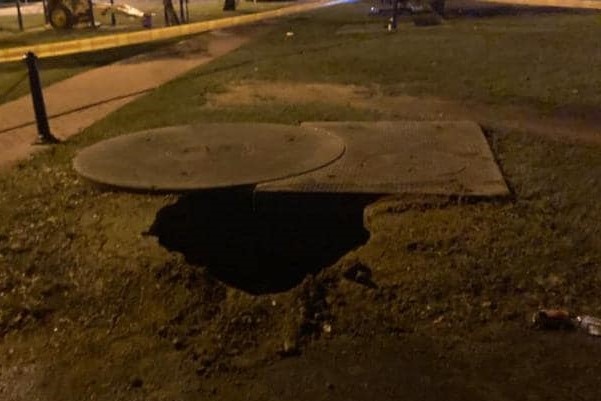 A large sinkhole in the ground near a pathway.